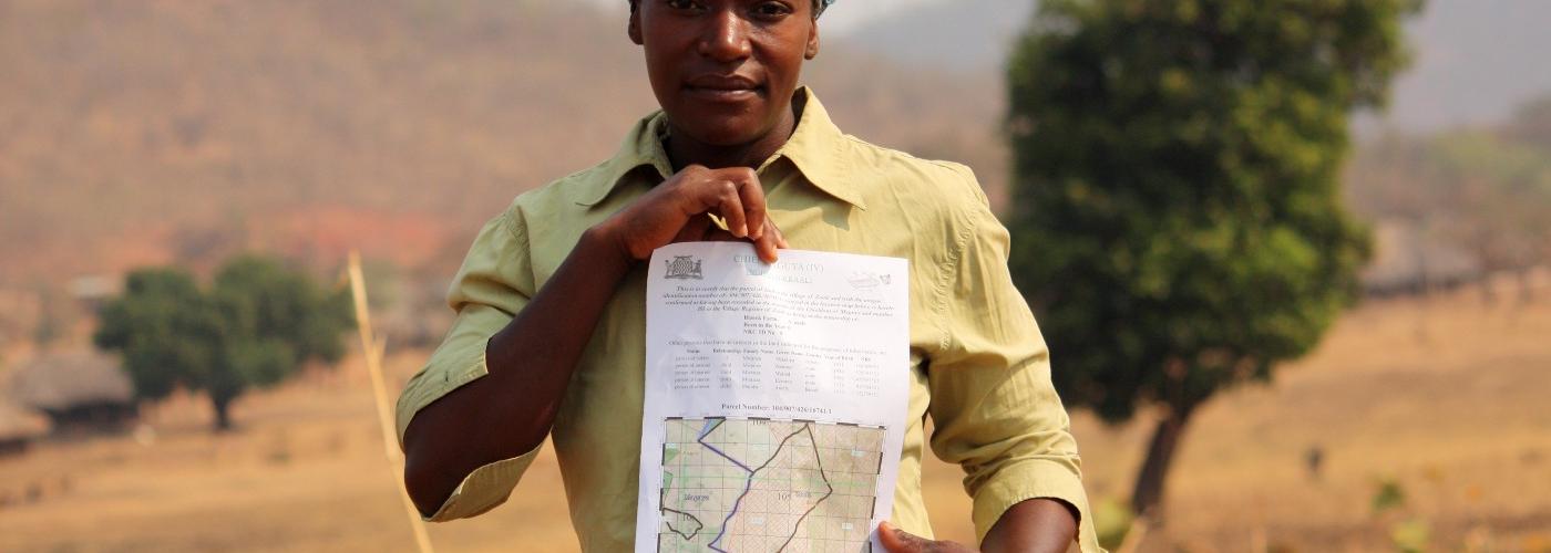 A woman looking at the camera, holding her customary land certificate on her parcel of land in eastern Zambia