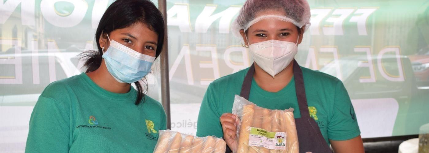 Two youth in green t-shirts and wearing masks are holding packaged food