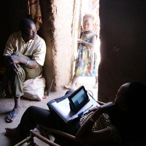 A man seated inside a home and a child outside at the entrance