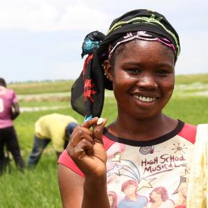 Young girl smiling at camera while standing on a farm holding up a seed