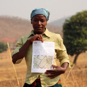 A woman looking at the camera, holding her customary land certificate on her parcel of land in eastern Zambia