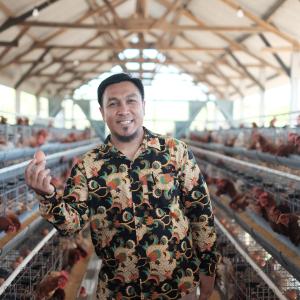 Man holds egg while standing inside a hen house in Indonesia. Photo: DAI Global. 
