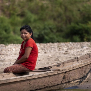 A woman sits on a fishing boat on the shoreline.